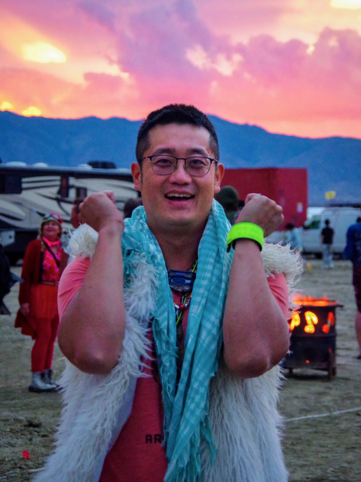 A camper cheering at sunset in a white fur vest and blue scarf