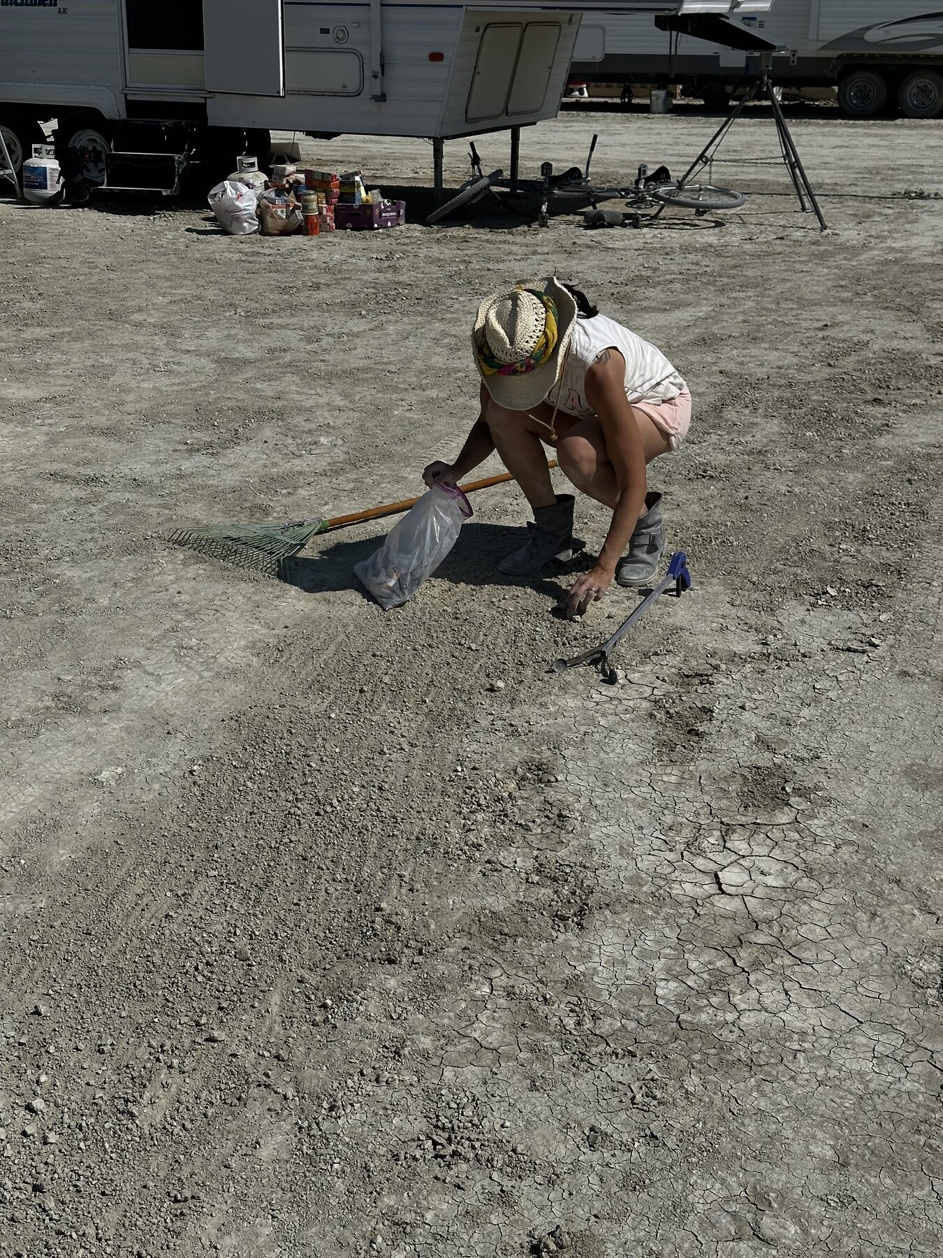 A camper crouched down picking debris out of the playa by hand
